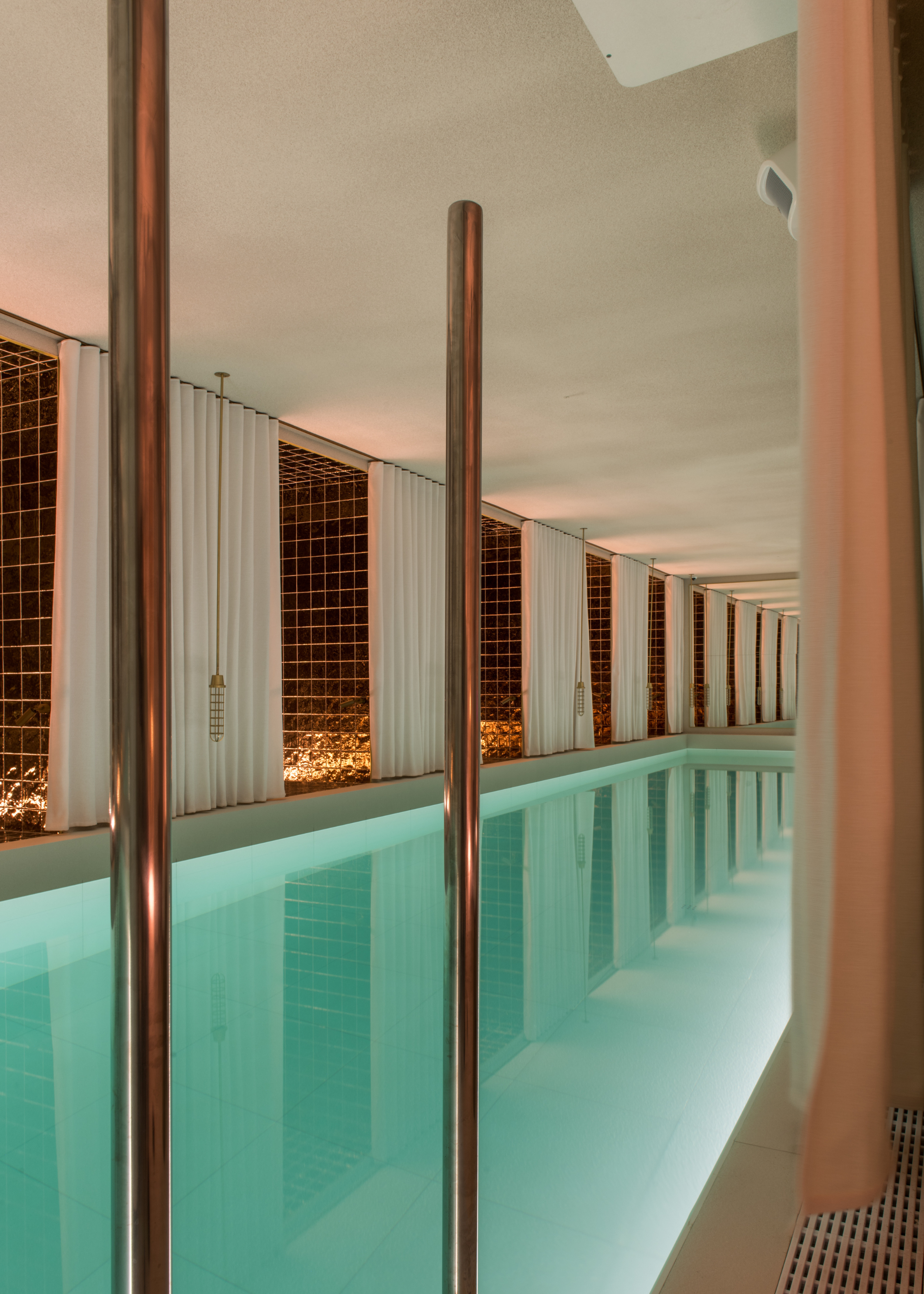 A white swimming pool with light blue tile and gold tiled accents with hanging pendants