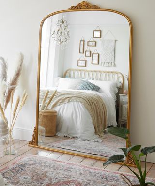 A large arched brass-colored decorative mirror in bedroom with pink traditional rug