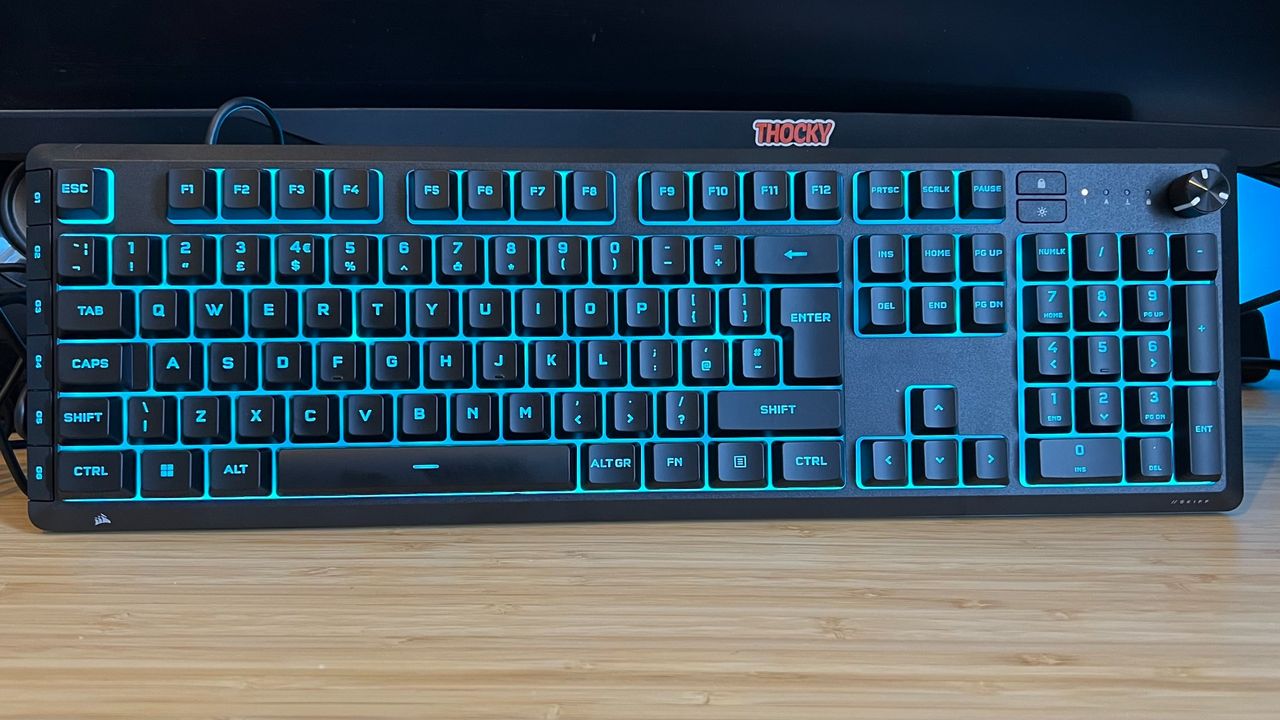 Corsair Skiff 100 Plus gaming keyboard standing upright with blue backlighting on a wooden desk