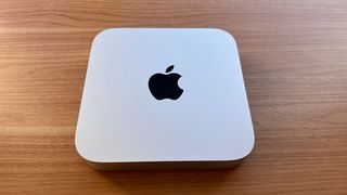 Photograph of a Mac mini (M2 Pro, 2023) from top showing Apple logo, on wooden surface