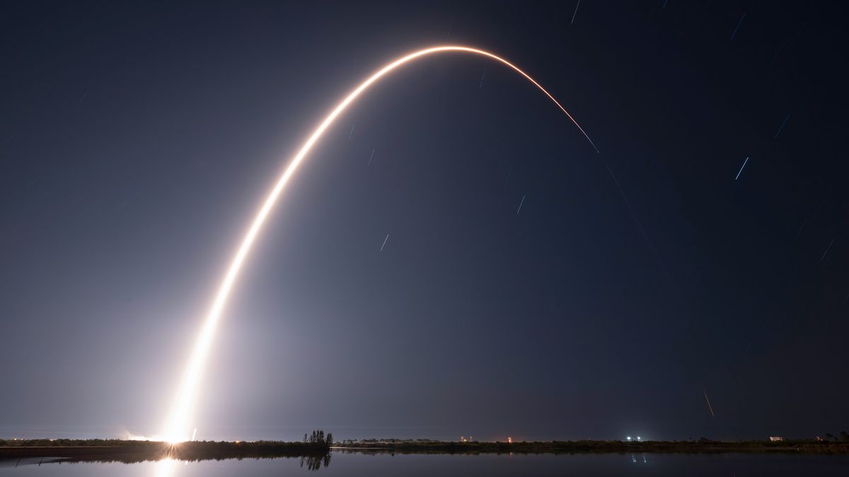 A rocket launch carves an orange arc into a dark night sky in this long-exposure photo.