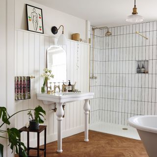 White tiled bathroom, shower, sink, mirror, and decorative items