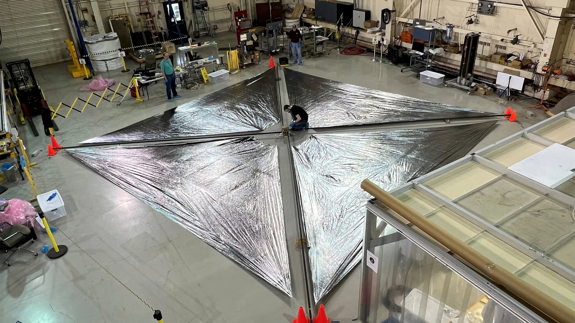 Four large shiny pieces of fabric lay on the floor in a testing facility.
