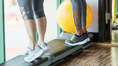 two pairs of legs stand on a workout step doing calf raises