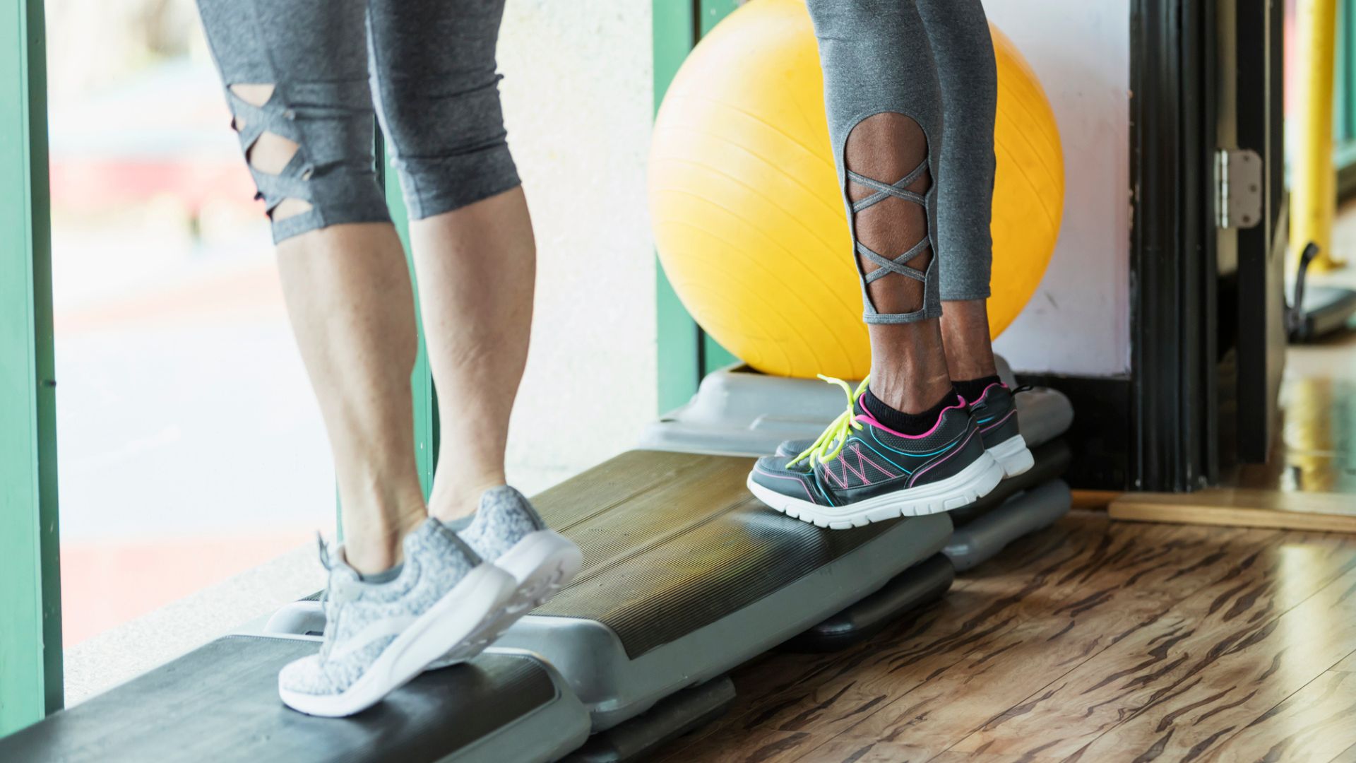 two pairs of legs stand on a workout step doing calf raises
