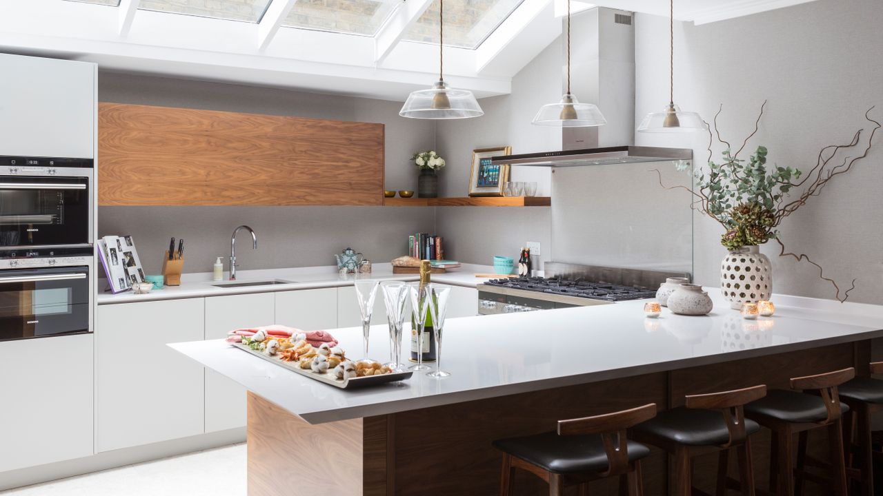 An example of U-shaped kitchen ideas illustrated by a sleek pale gray scheme with skylights and pendant lighting.