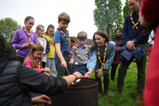 Princess Charlotte, Prince George, Prince Louis and Kate Middleton roasting marshmallows around a fire while Prince William looks on