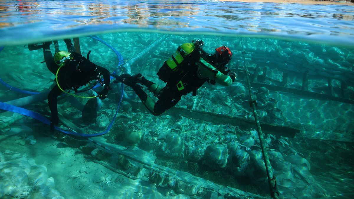 Scuba divers swim in shallow water to observe the shipwreck