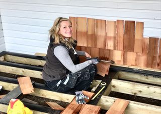 TV presenter Sian Astley smiling at the camera midway through nailing wood cladding to an exterior wall