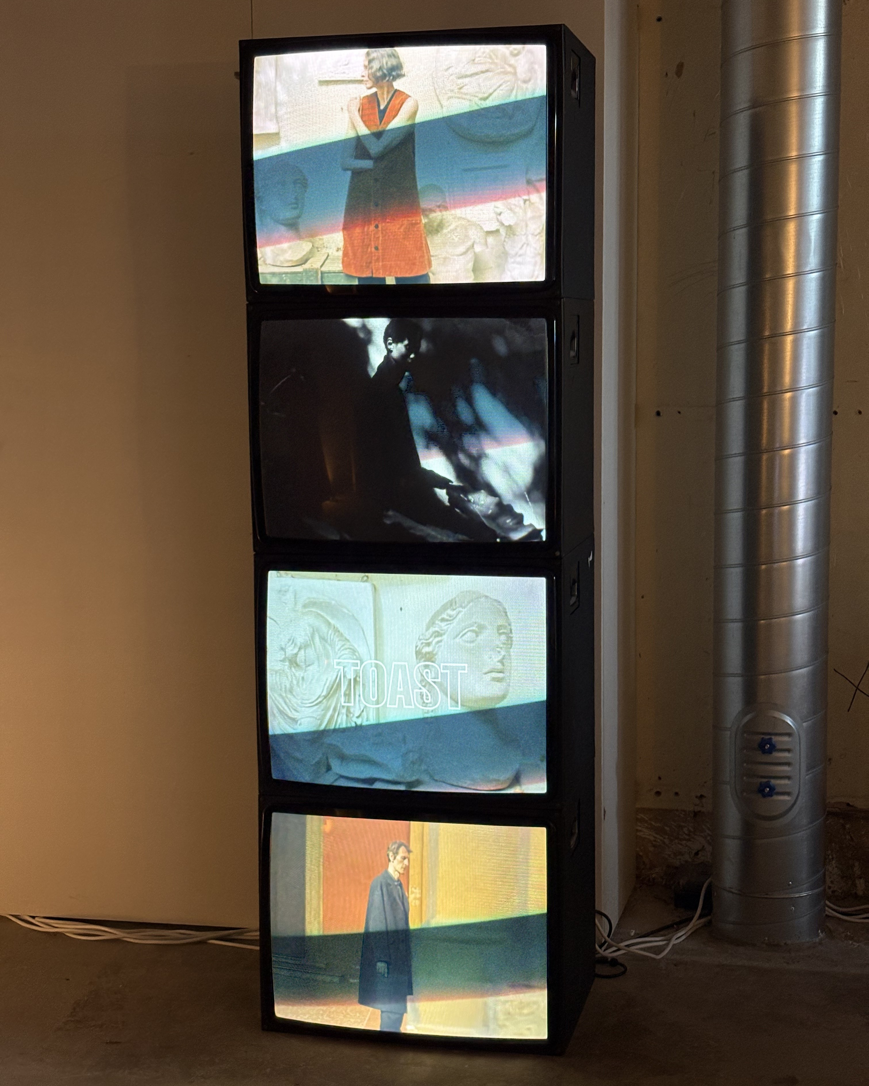 Installation view of a fashion and design exhibition featuring clothes, homeware, retro-looking tvs showcasing audiovisual works, large posters, and more.