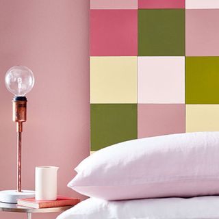 Light pink painted wall with light on the pedestal next to bed with white pillow