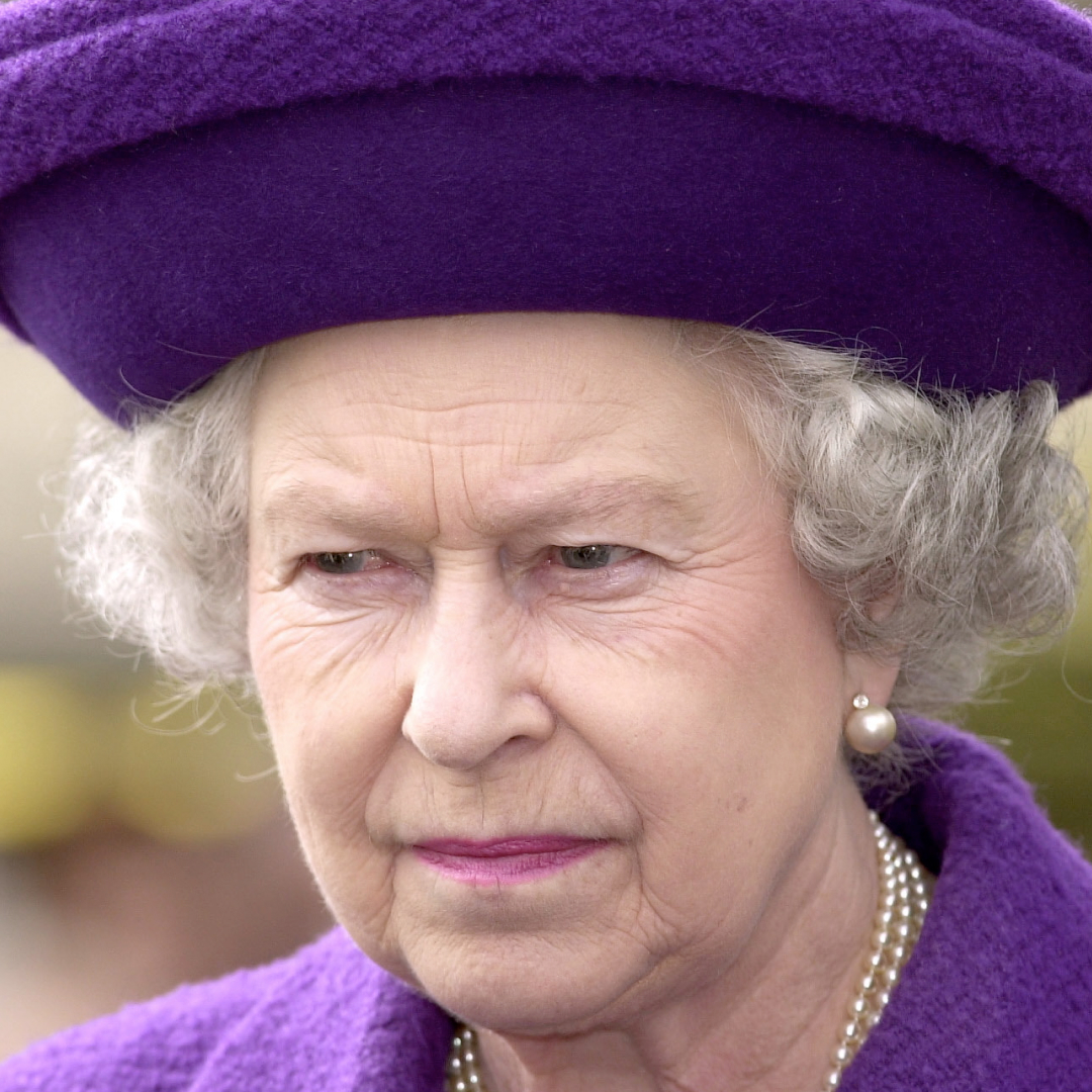 Queen Elizabeth wearing a purple hat and coat scowling