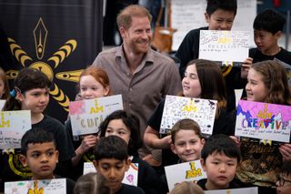 Prince Harry smiling surrounded by a group of children holding up colorful signs