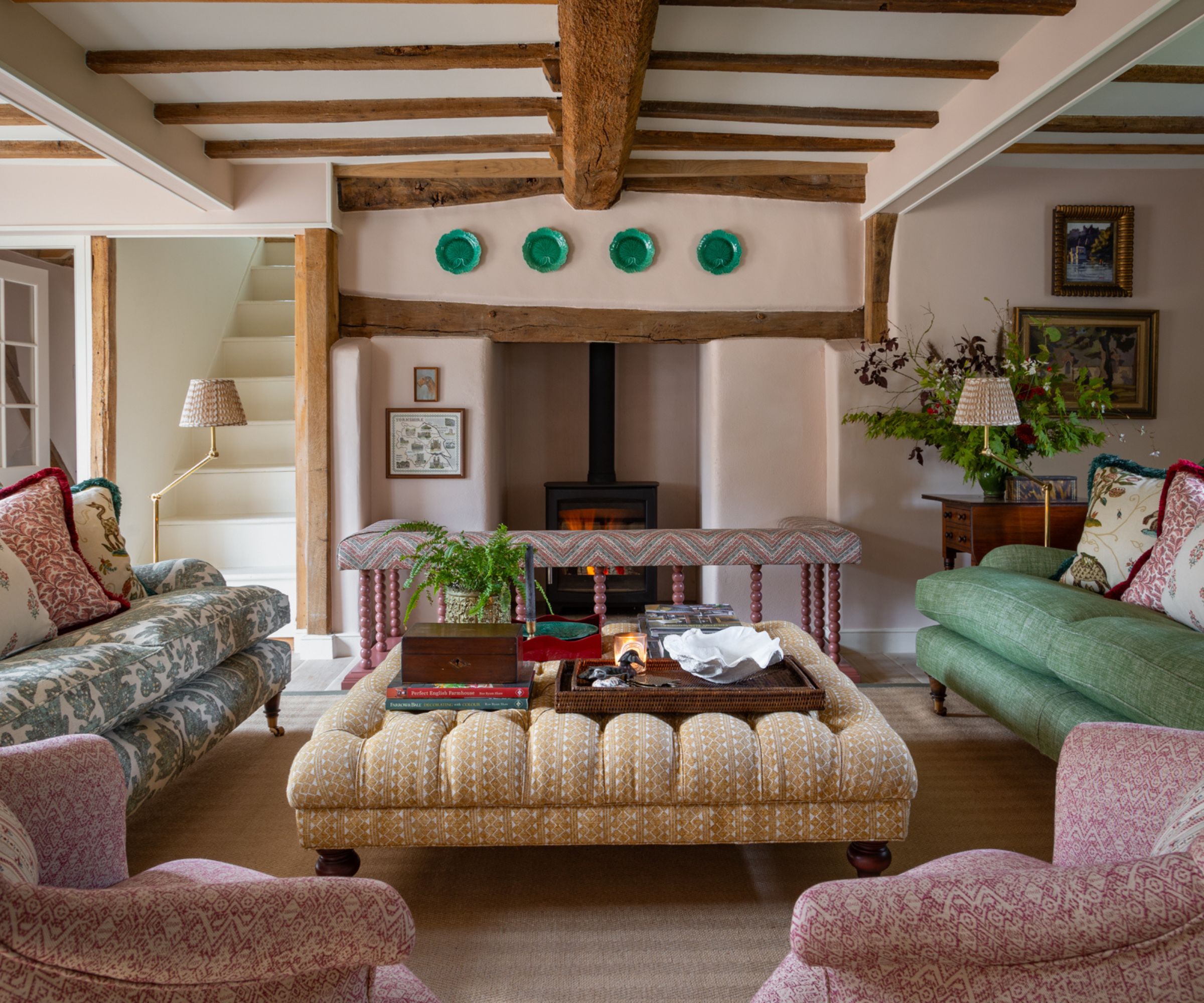 pale pink cottage living room with traditional english style, wooden beams, fireplace, and eclectic mismatched upholstered furniture