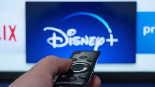 A person points a remote at their TV on which the Disney Plus logo is displayed