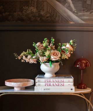 dark brown wall with console table with vase of flowers, stack of books, decorative tray, and red lamp