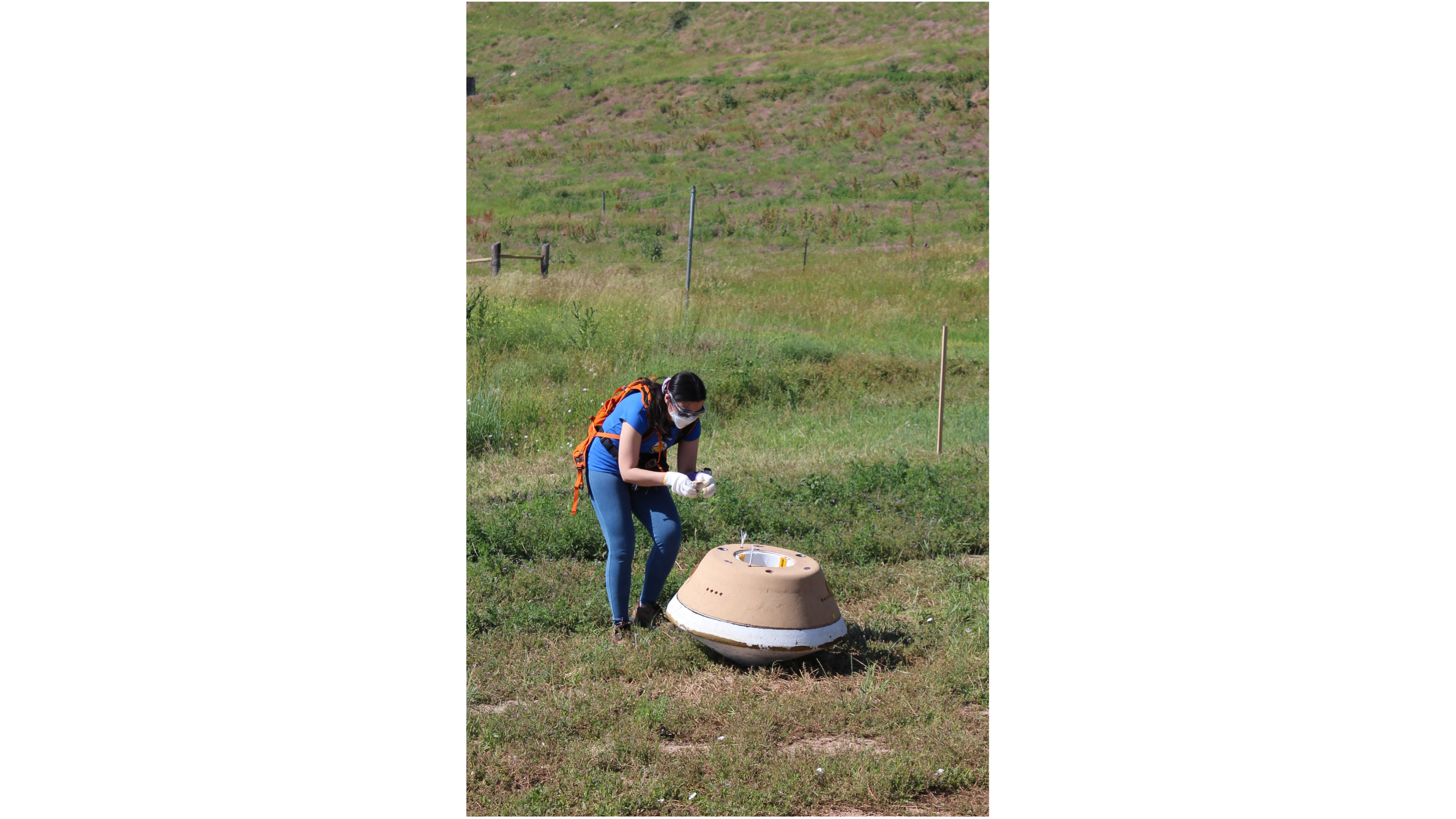 a woman examines a cylindrical mock space capsule in a grassy field