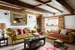 living room with gold velvet sofas red cushions and beams and limewashed walls and dark coffee table