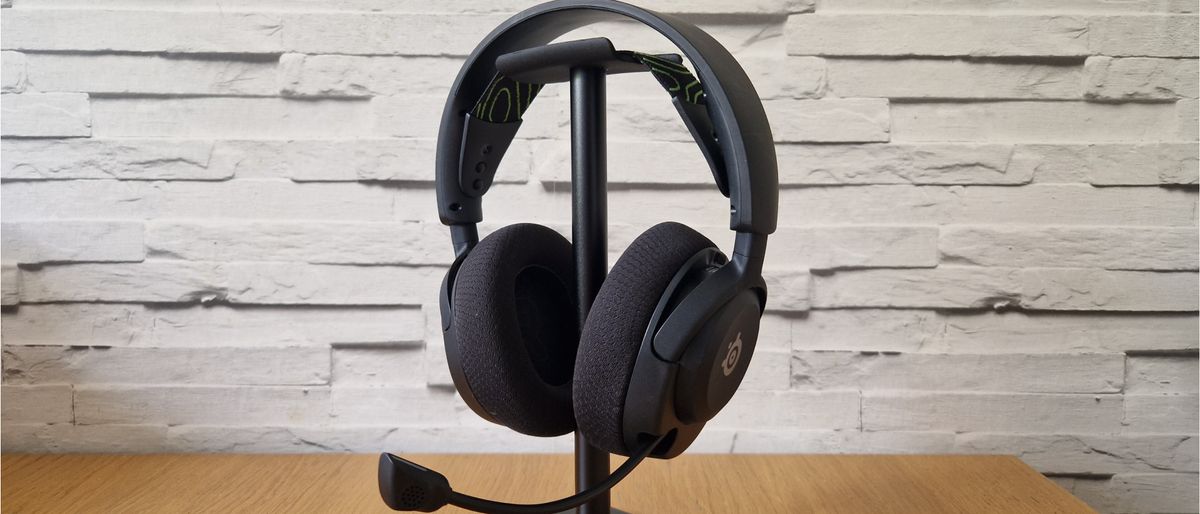 The SteelSeries Arctis Nova 5 gaming headset on a stand in front of a white brick background