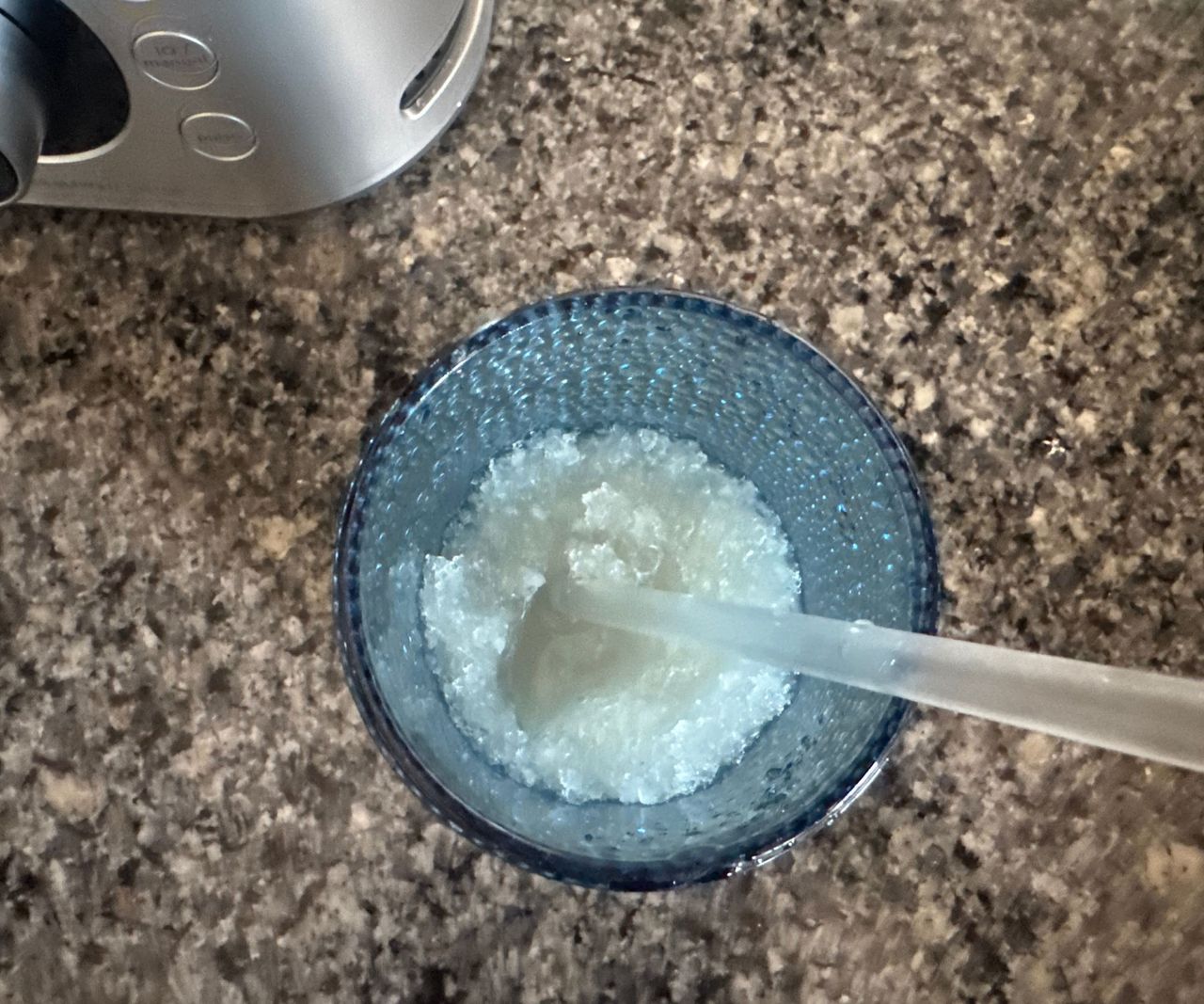 Finely crushed ice inside a blue glass with a straw, viewed rom above.