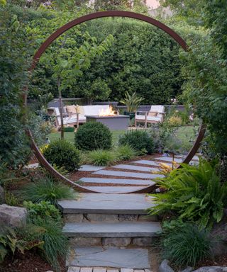 A circular garden sculpture with steps surrounded by foliage