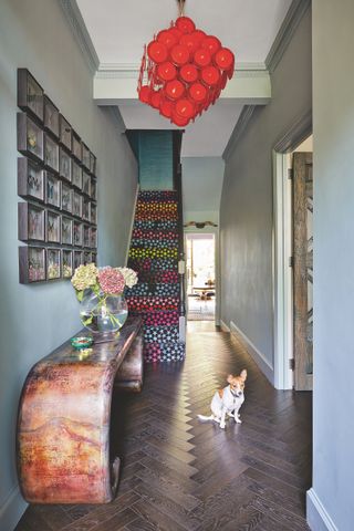 Hallway with parquet floor grey wall with artwork, console table and stair carpet with bold pattern