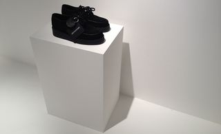 White floor and wall, white block platform with a pair of black lace up shoes on display