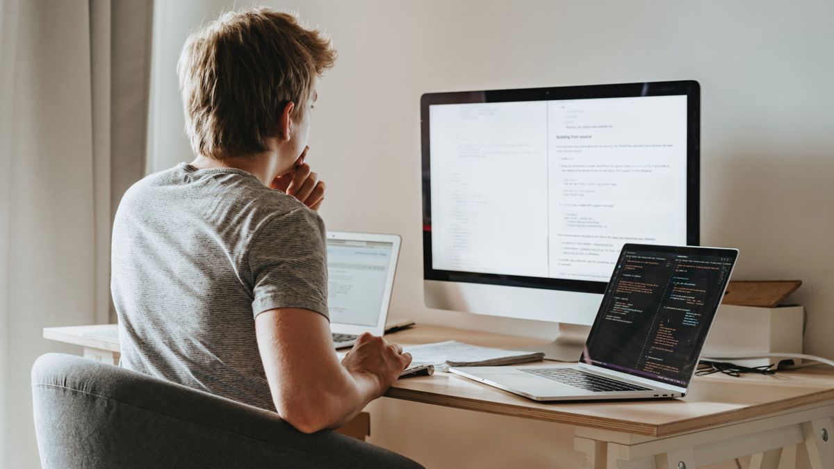 Man looking at three different computer screens at desk