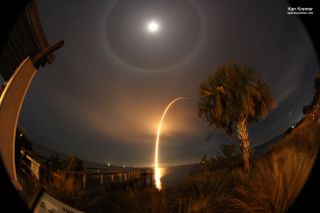 the full moon can be seen in the sky above an arc formed by a rocket launch