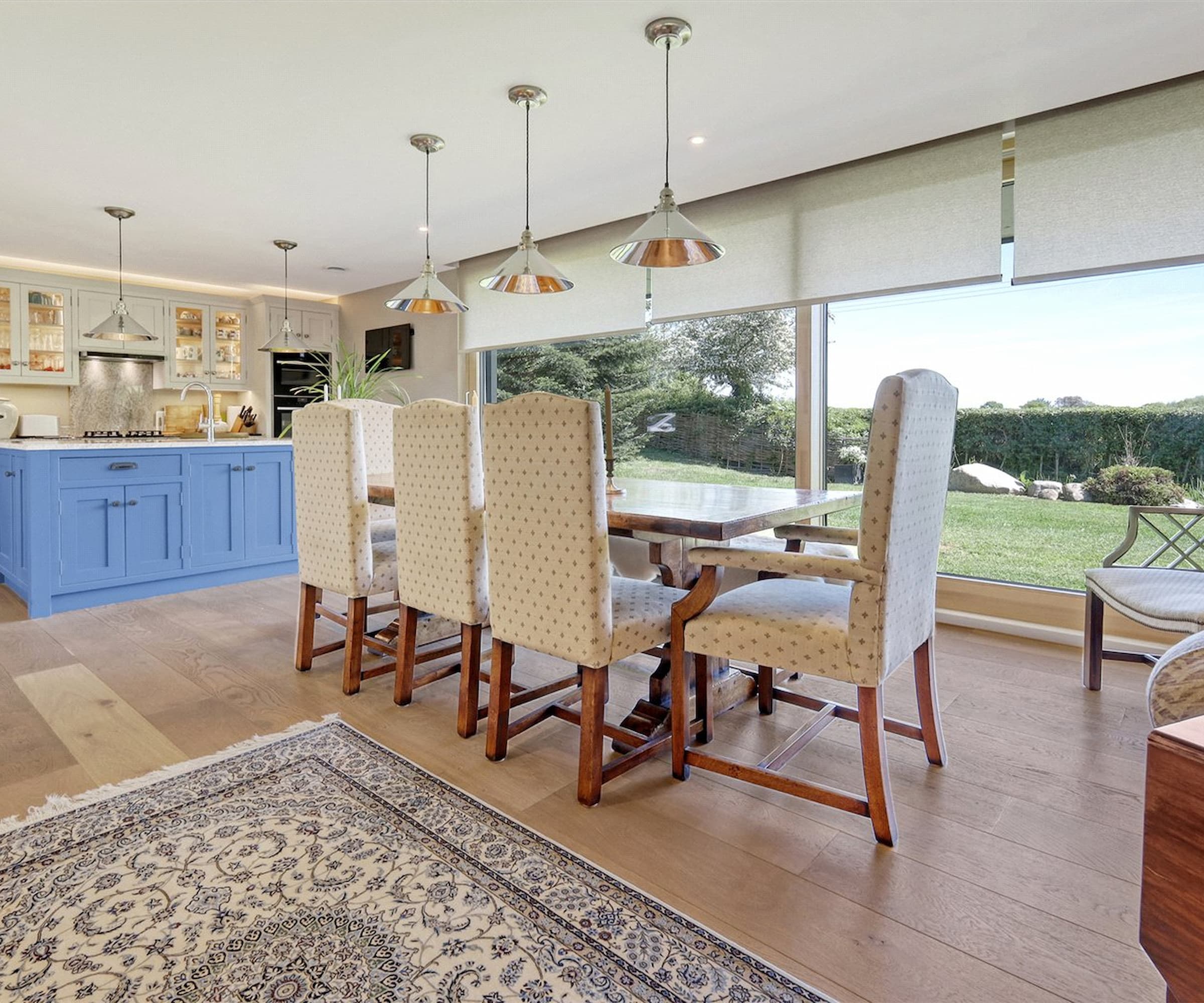 A dining area with wooden kitchen table and tall picture windows with blinders
