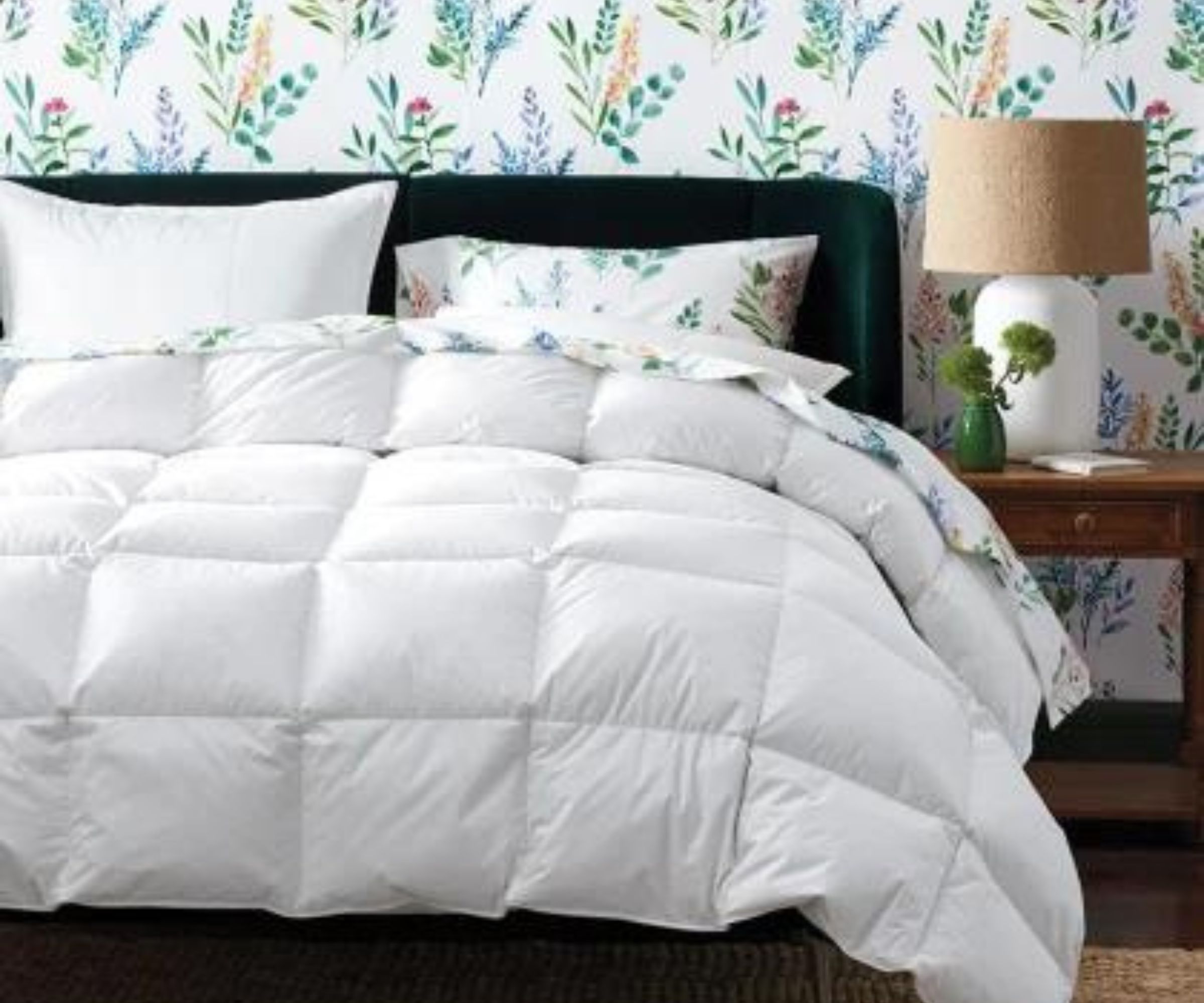 The Company Store Premium Alberta Down Comforter on a bed against floral wallpaper.