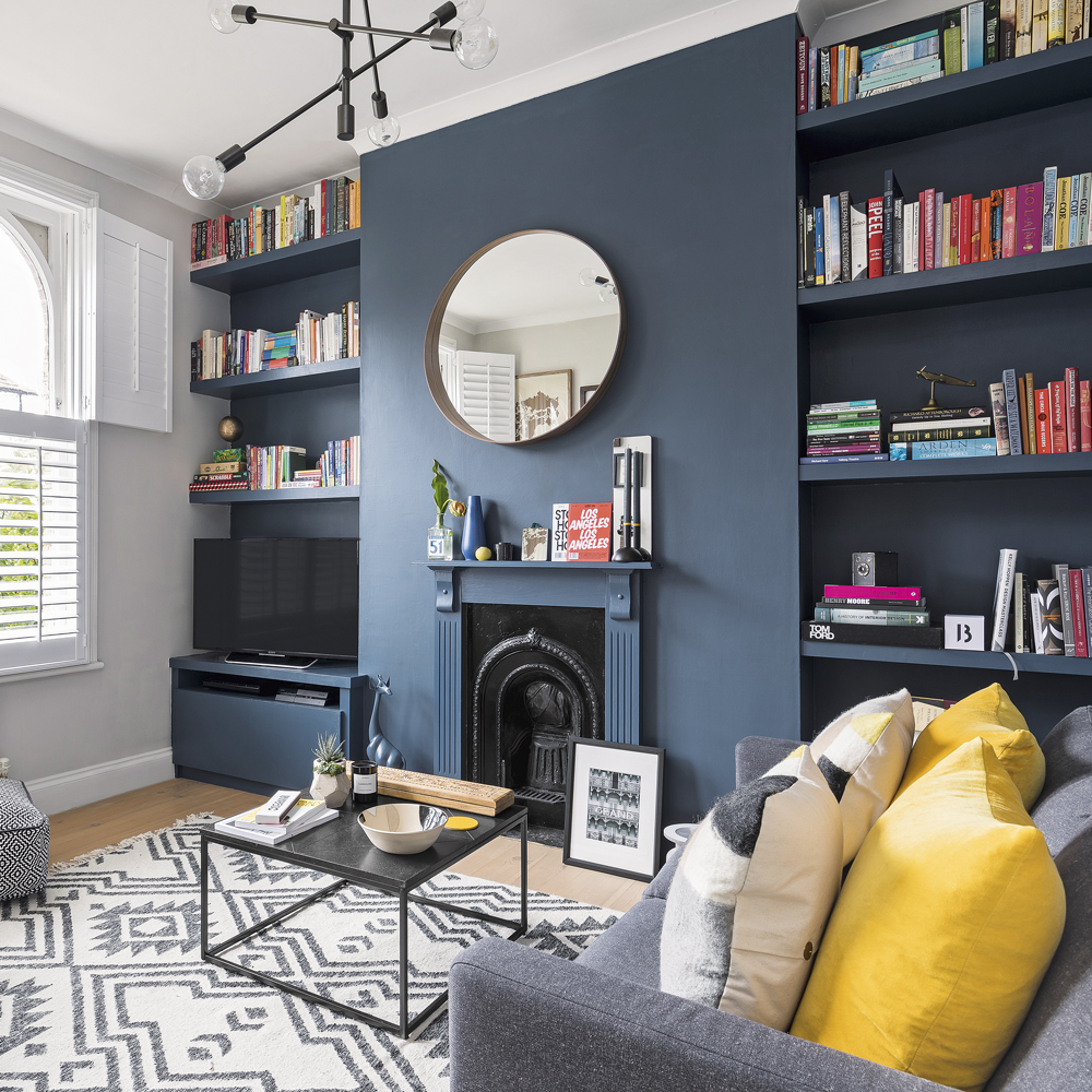 A living room with a navy feature wall with bookcases and a round mirror