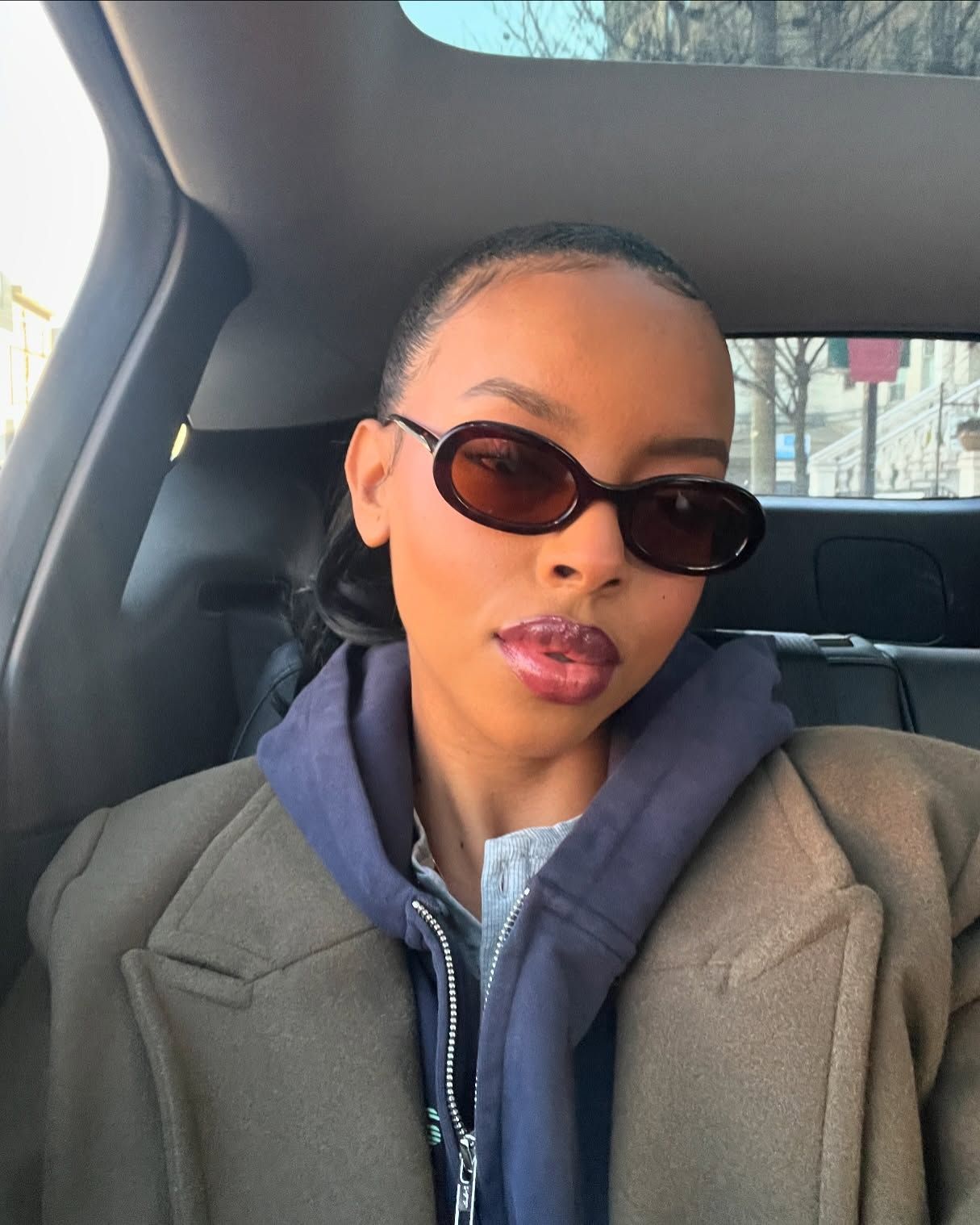 Woman taking selfie in car with a slicked-back bun and sunglasses