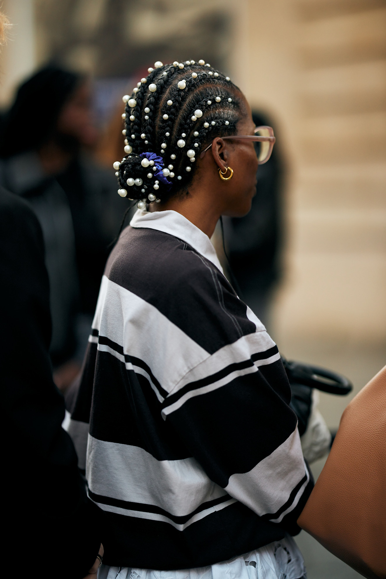 a woman with cornrows and a bun with pearls in her hair wearing a stripe rugby shirt facing away from the camera