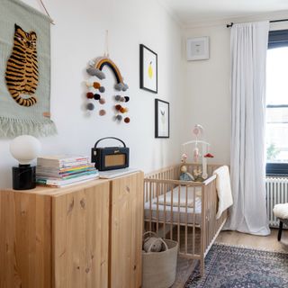 Wooden crib, wooden chest of drawers with hanging tiger tapestry and felt rainbow above