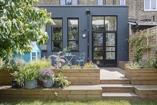 Rear extension with black metal cladding and black aluminium industrial-style windows and French doors leading onto decking with seating area