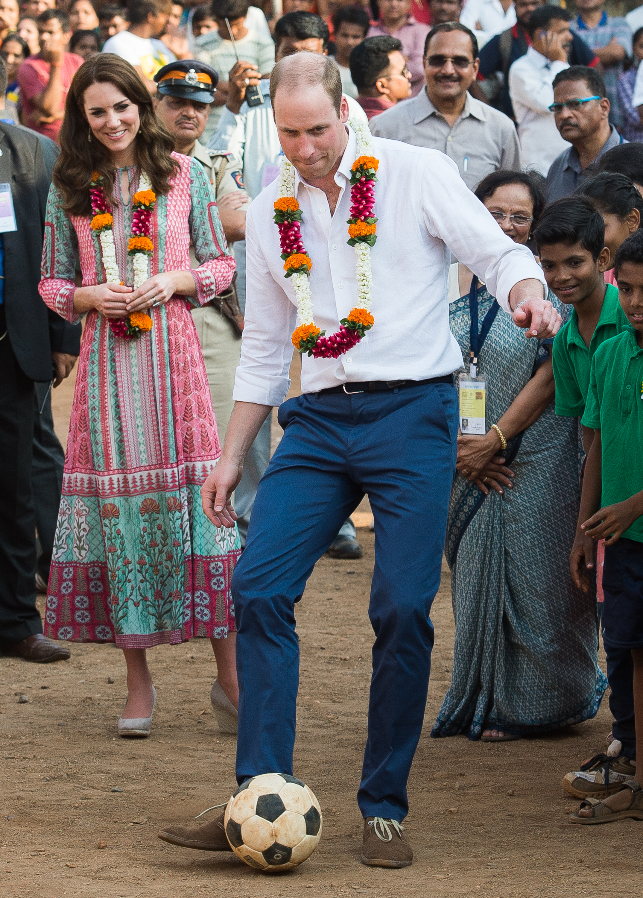 Prince William kicking a soccer ball in India with Princess Kate watching behind