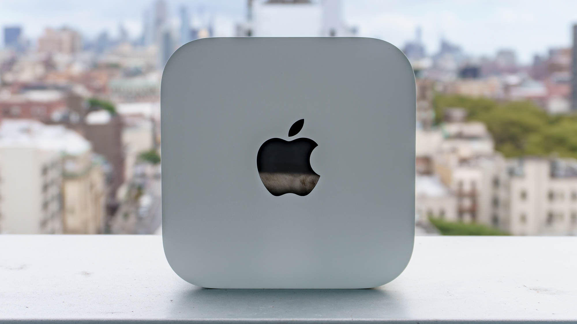 A Mac Mini with M6 upright on its side showing the Apple logo with a cityscape in the background
