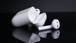 Earpods on a black reflective surface in front of a gray background