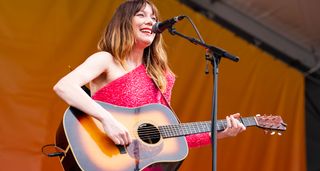 Molly Tuttle plays a sunburst dreadnought onstage and wears a pink sparkly dress as she performs at the 2024 New Orleans Jazz & Heritage Festival.