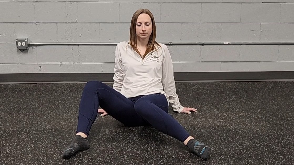 Woman demonstrating stretch. She wears a white long-sleeve top, blue sports leggings and black socks