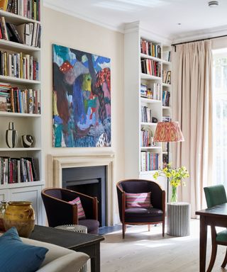 A living room with a large piece of artwork above a fireplace, large built-in bookshelves on either side, and seating