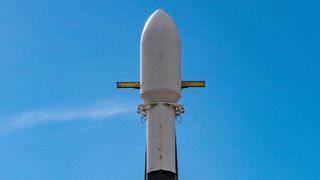 the top of a white rocket is seen with the arms of its transporter-erector extended out from behind.