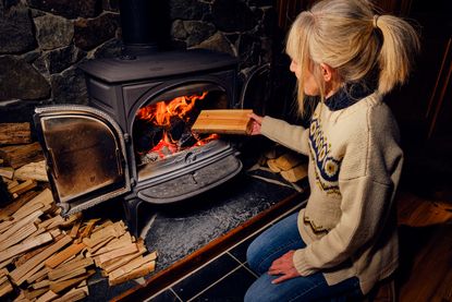 Woman putting a log into a wood burning stove