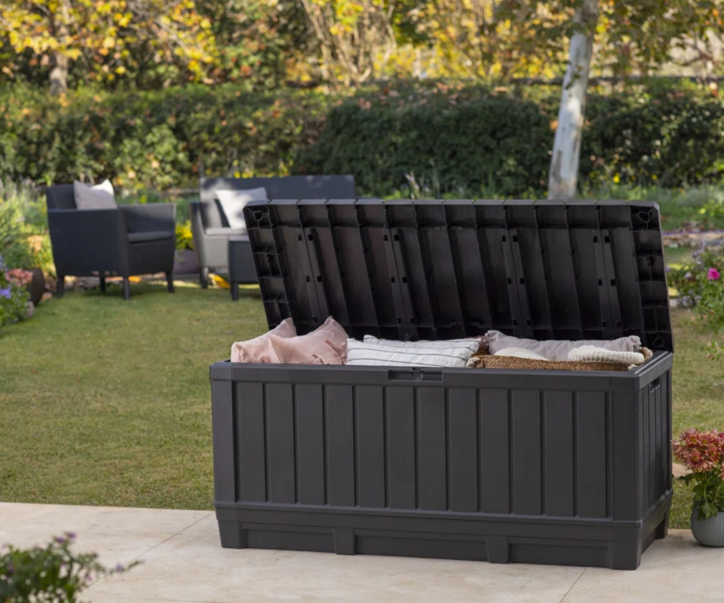 A large black outdoor storage box on a patio, it&#039;s filled with outdoor cushions
