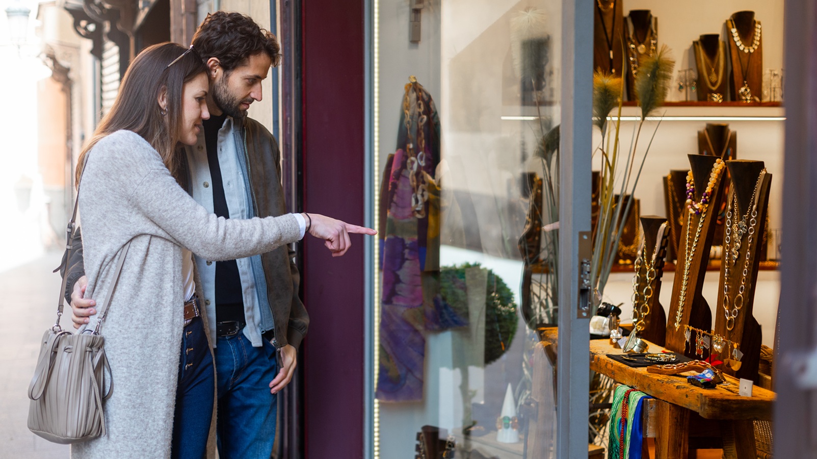Young couple smiling and pointing at beautiful jewelry displayed in a shop window, sharing a moment of joy and desire for luxury items