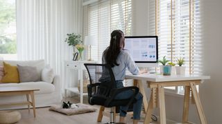 Hybrid working concept image showing woman working at a computer desk in her home.