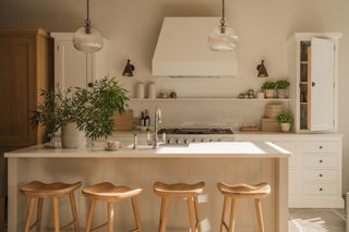 a white neptune kitchen with wood bar stools around an island