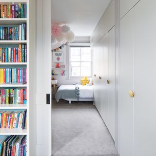 A girls' bedroom with flush white wardrobes, bed, plush yellow star pillow decor and bookshelf outside of bedroom