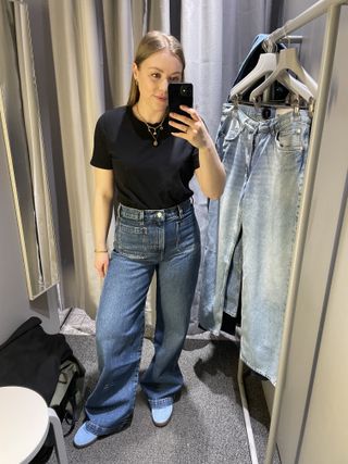 Woman in dressing room wearing black t-shirt, blue jeans, blue trainers